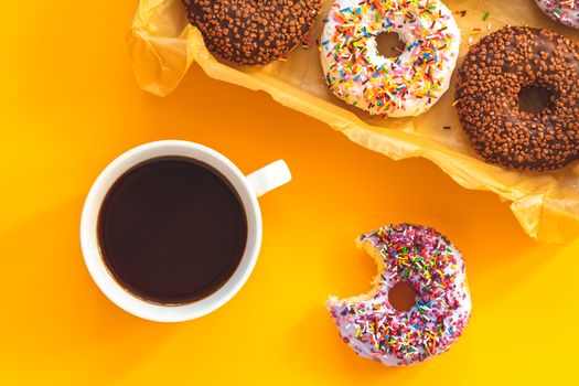 Delicious glazed donuts in box and cup of coffee on yellow surface. Flat lay minimalist food art background. Top view.