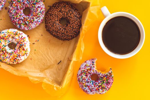 Delicious glazed donuts in box and cup of coffee on yellow surface. Flat lay minimalist food art background. Top view.
