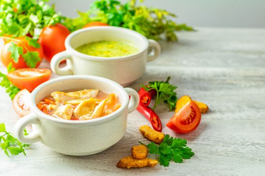 Concept of healthy vegetable and legume soups. Vegetables soup with carrot, eggs and chicken, mushroom cream soup with herbs and crackers and ingredients. Top view on the background of a light gray wooden board, copy space.