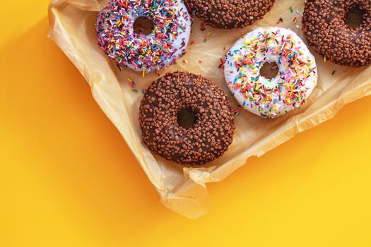Delicious glazed donuts in box on yellow surface. Flat lay minimalist food art background. Top view.