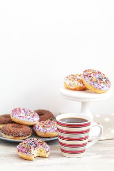 Delicious glazed donuts and cup of coffee on light wooden background. Beautiful romantic breakfast or lunch concept. Shallow depth of the field.