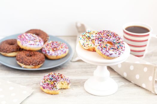 Delicious glazed donuts and cup of coffee on light wooden background. Beautiful romantic breakfast or lunch concept. Shallow depth of the field.