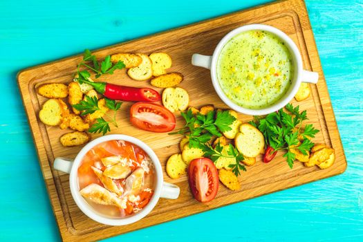 Concept of healthy vegetable and legume soups. Vegetables soup with carrot, eggs and chicken, mushroom cream soup with herbs and crackers and ingredients. Top view, blue turquoise wooden, copy space