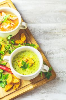 Concept of healthy vegetable and legume soups. Vegetables soup with carrot, eggs and chicken, mushroom cream soup with herbs and crackers and ingredients. Background of a light gray board, copy space