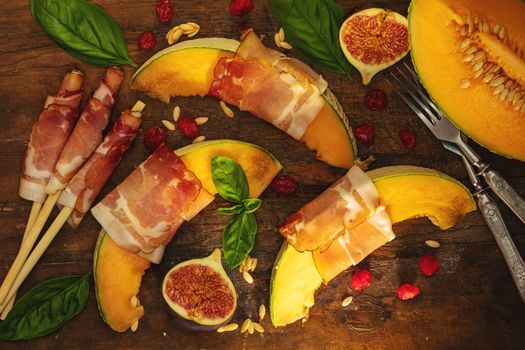 Cantaloupe melon sliced with Prosciutto jamon, basil leaves, fig and dried cherry. Italian appetizer on wooden background.