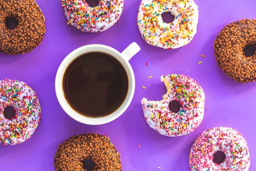 Delicious glazed donuts and cup of coffee on violet surface. Flat lay minimalist food art background. Top view.