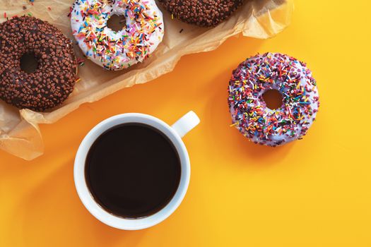 Delicious glazed donuts in box and cup of coffee on yellow surface. Flat lay minimalist food art background. Top view.