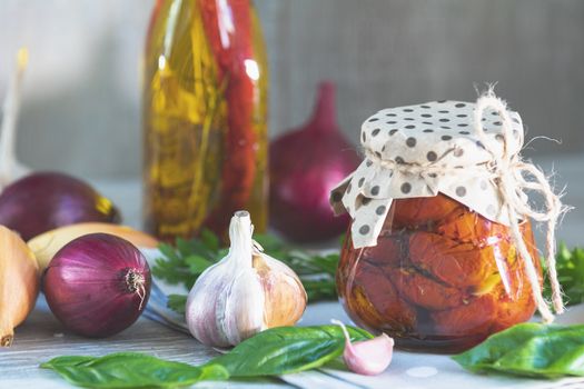 Sun dried tomatoes in glass jar, onion, basil leaves and garlic on cutting board, on wooden background