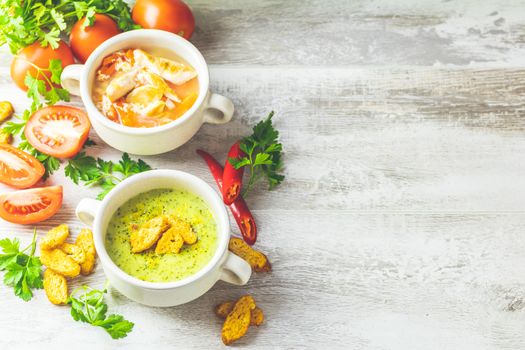 Concept of healthy vegetable and legume soups. Vegetables soup with carrot, eggs and chicken, mushroom cream soup with herbs and crackers and ingredients. Background of a light gray board, copy space