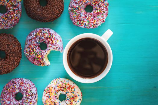 Delicious glazed donuts and cup of coffee on turquoise blue surface. Flat lay minimalist food art background. Top view.