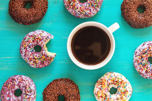 Delicious glazed donuts and cup of coffee on turquoise surface. Flat lay minimalist food art background. Top view.