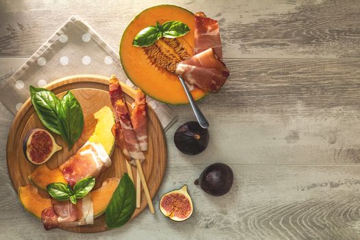 Cantaloupe melon sliced with Prosciutto jamon, basil leaves, fig and dried cherry. Italian appetizer on wooden background.