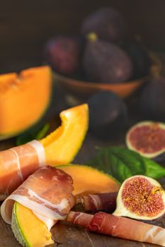 Cantaloupe melon sliced with Prosciutto jamon, basil leaves, fig and dried cherry. Italian appetizer on wooden background.