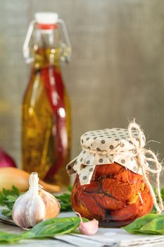 Sun dried tomatoes in glass jar, onion, basil leaves and garlic on cutting board, on wooden background