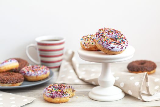 Delicious glazed donuts and cup of coffee on light wooden background. Beautiful romantic breakfast or lunch concept. Shallow depth of the field.