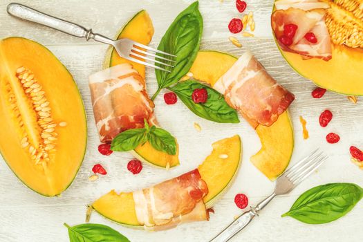 Cantaloupe melon sliced with Prosciutto jamon, basil leaves, fig and dried cherry. Italian appetizer on wooden background