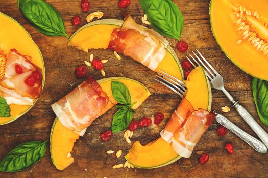 Cantaloupe melon sliced with Prosciutto jamon, basil leaves, fig and dried cherry. Italian appetizer on wooden background.