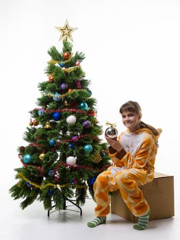 A girl sits on a box for storing Christmas decorations and holds a ball in her hands