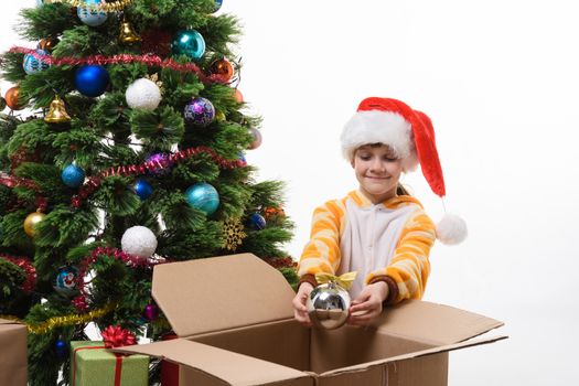 A girl decorates a Christmas tree and takes out Christmas toys from a box