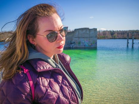 young woman with red jacket and abndoned Quarry Of Rummu, Estonia on the background. Scenic View Of Land Against Clear Blue Sky. Panoramic View.