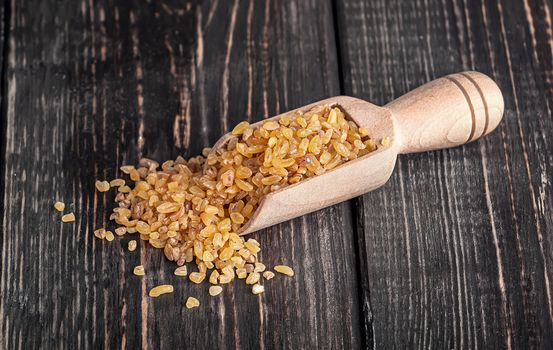 Bulgur in wooden scoop on dark table