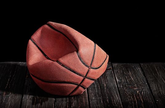 Deflated and rumpled old ball on a wooden floor. Black background.