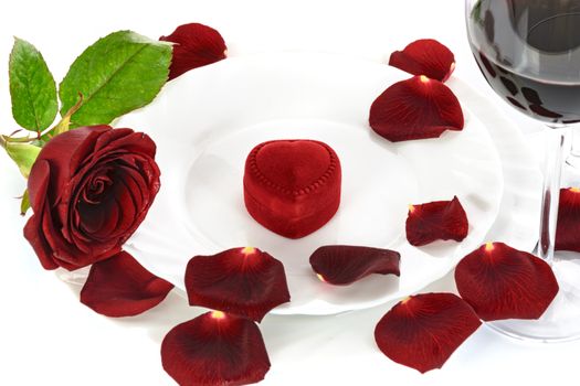 Table setting for a romantic Valentines Day dinner with a red rose, red wine and gift.
