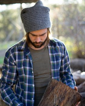 Portrait of young bearded man taking a log of wood with beautiful sunlight
