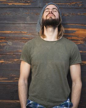 Portrait of young bearded man while he is meditating with a wood background