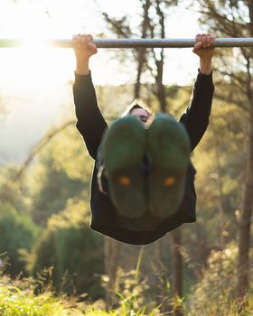 Young bearded man doing pull ups in the park with beautiful sunset on the mountain