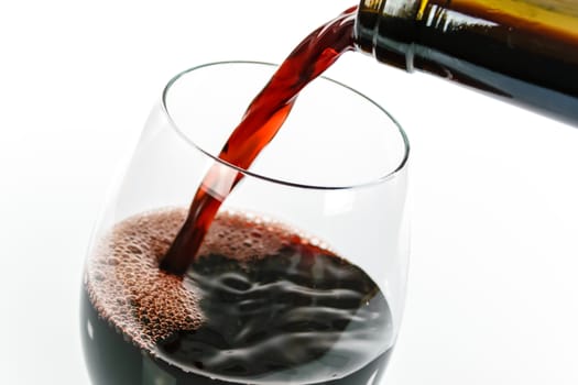 Pouring red wine into a wineglass isolated on white background.