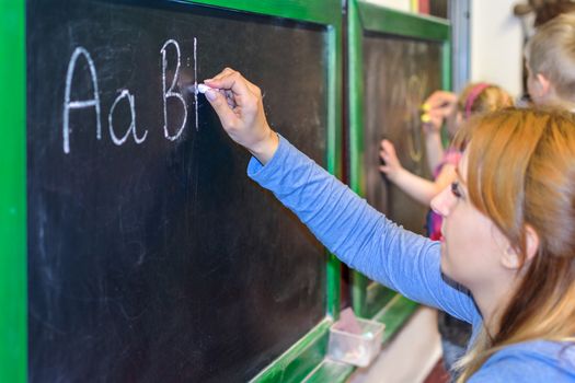 Teacher shows the children how to write alphabet letters on the blackboard at school