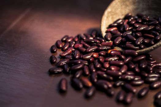 Close up of raw kidney beans on brown colored surface in a clay bowl with a spotlight on it. Horizontal shot.