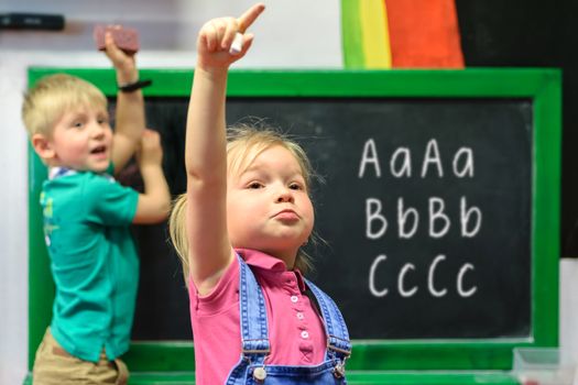 Beautiful little girl and boy learn to write on the blackboard in kindergarten