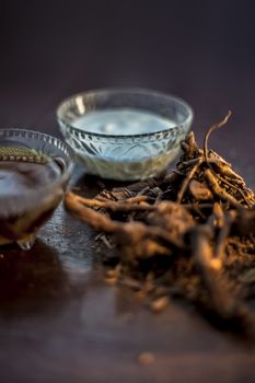 Raw ayurvedic herb chitrak/Plumbago zeylanica roots on the brown-colored shiny surface with some buttermilk, ghee or clarified butter, its extract, curd, and honey with it used in ayurvedic therapy.