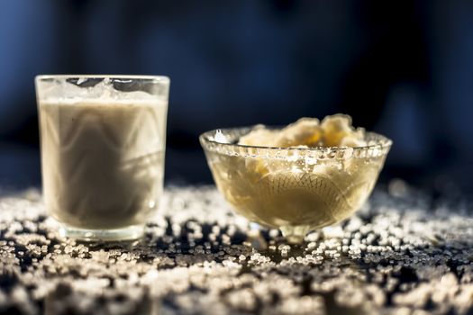 Close up of glass bowl of pure milk well mixed with hot milk in it on black wooden glossy surface along with raw ghee clarified butter and some sugar crystals spread on the surface. Horizontal shot.