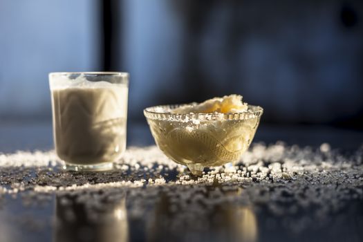 Close up of glass bowl of pure milk well mixed with hot milk in it on black wooden glossy surface along with raw ghee clarified butter and some sugar crystals spread on the surface. Horizontal shot.