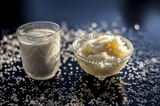 Close up of glass bowl of pure milk well mixed with hot milk in it on black wooden glossy surface along with raw ghee clarified butter and some sugar crystals spread on the surface. Horizontal shot.