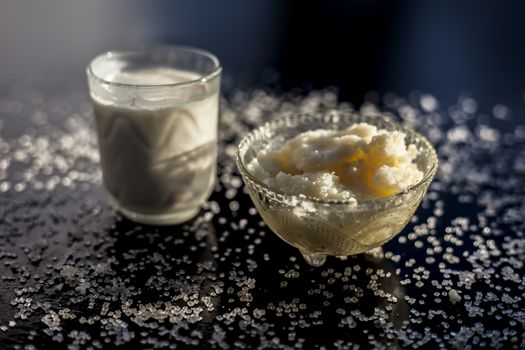 Close up of glass bowl of pure milk well mixed with hot milk in it on black wooden glossy surface along with raw ghee clarified butter and some sugar crystals spread on the surface. Horizontal shot.