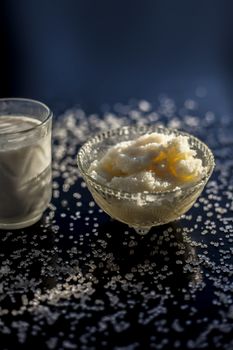 Close up of glass bowl of pure milk well mixed with hot milk in it on black wooden glossy surface along with raw ghee clarified butter and some sugar crystals spread on the surface. Vertical shot.