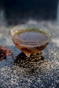 Close up of a glass bowl full of organic honey used in spa on black glossy surface with some white crystals spread on the surface. Vertical shot.