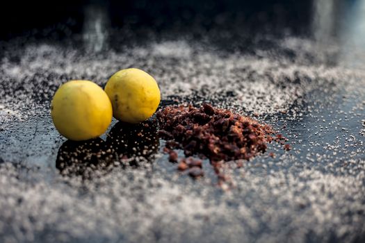 Pair of raw organic ripe yellow lemons on a black surface along with some rock salt (sendha namak) and white or common salt spread on the surface. Used for the salt remedy of skin and as a face mask.