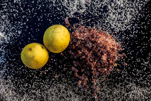 Pair of raw organic ripe yellow lemons on a black surface along with some rock salt (sendha namak) and white or common salt spread on the surface. Used for the salt remedy of skin and as a face mask.