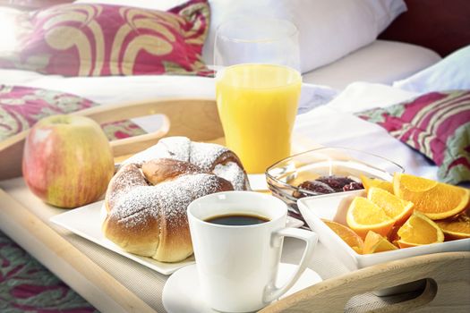 Shot on hotel's breakfast tray with croissants, coffee, oranges, juice, jam, apple and cutlery (reduced tone)
