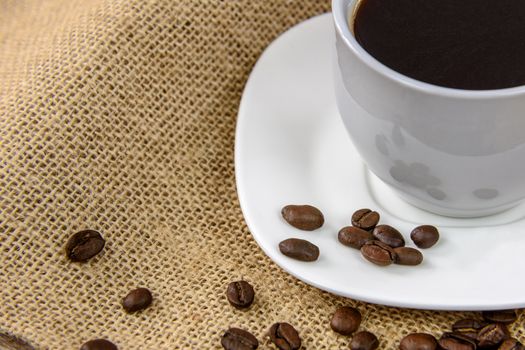 Cup of coffee with roasted beans on a burlap sack.