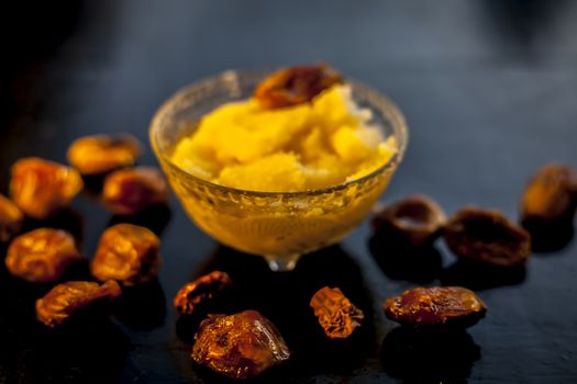 Close up shot of dates soaked in ghee for better stamina and health on black wooden surface along with ghee or clarified butter. Horizontal shot.