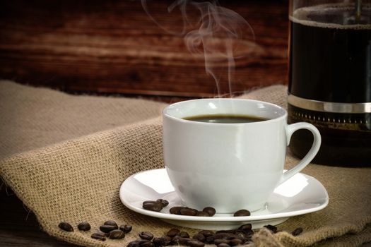 Cup of coffee with roasted beans and coffee maker on a burlap sack.