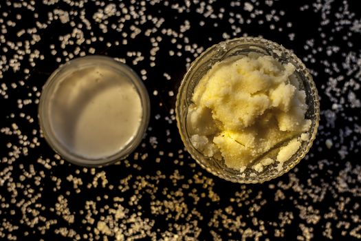 Close up of glass bowl of pure milk well mixed with hot milk in it on black wooden glossy surface along with raw ghee clarified butter and some sugar crystals spread on the surface. Horizontal shot.;