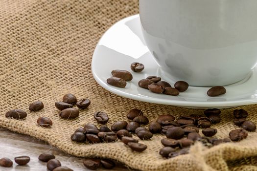 Cup of coffee with roasted beans on a burlap sack.