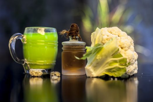 Close up shot of raw fresh cauliflower along with its juice and extracted essential oil on black surface.